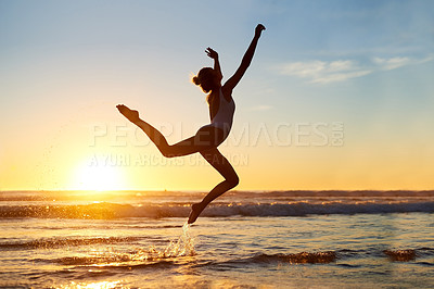 Buy stock photo Shot of a young woman jumping into mid air against a beautiful sunset at the beach