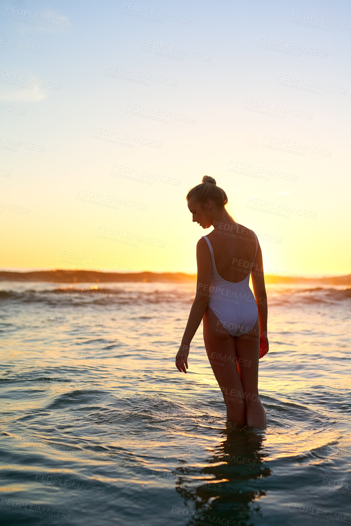 Buy stock photo Shot of a young woman standing in the water at sunset