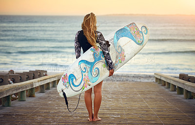 Buy stock photo Rearview shot of an unrecognizable young female surfer standing with her surfboard looking over the ocean