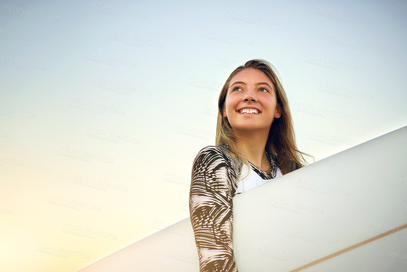 Buy stock photo Low angle shot of an attractive young female surfer standing with her surfboard on the beach