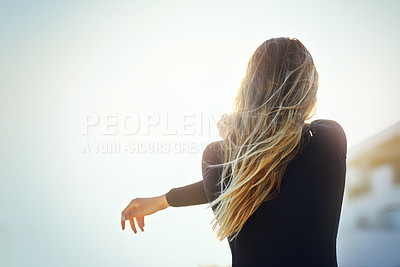 Buy stock photo Rearview shot of an unrecognizable young female surfer warming up on the beach