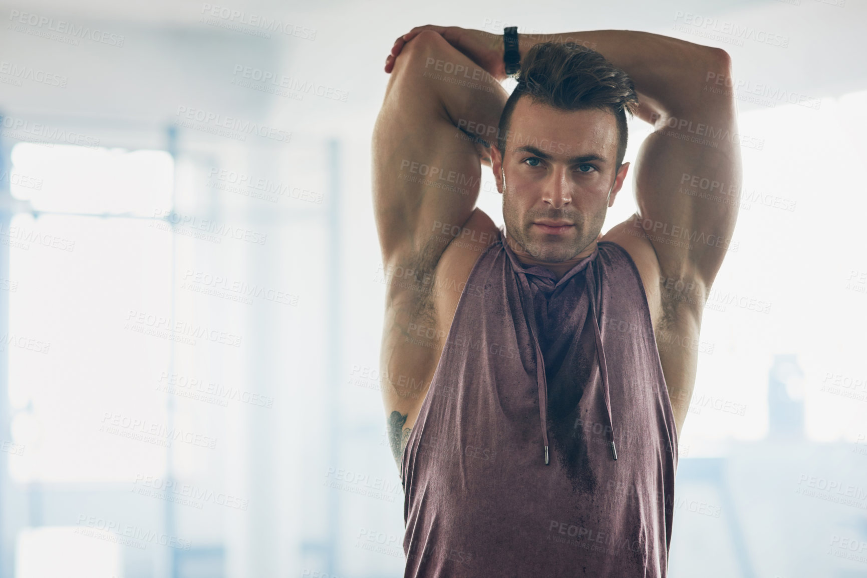 Buy stock photo Shot of a handsome young man stretching at the gym