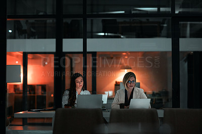Buy stock photo Shot of two colleagues using their laptops during a late night in a modern office