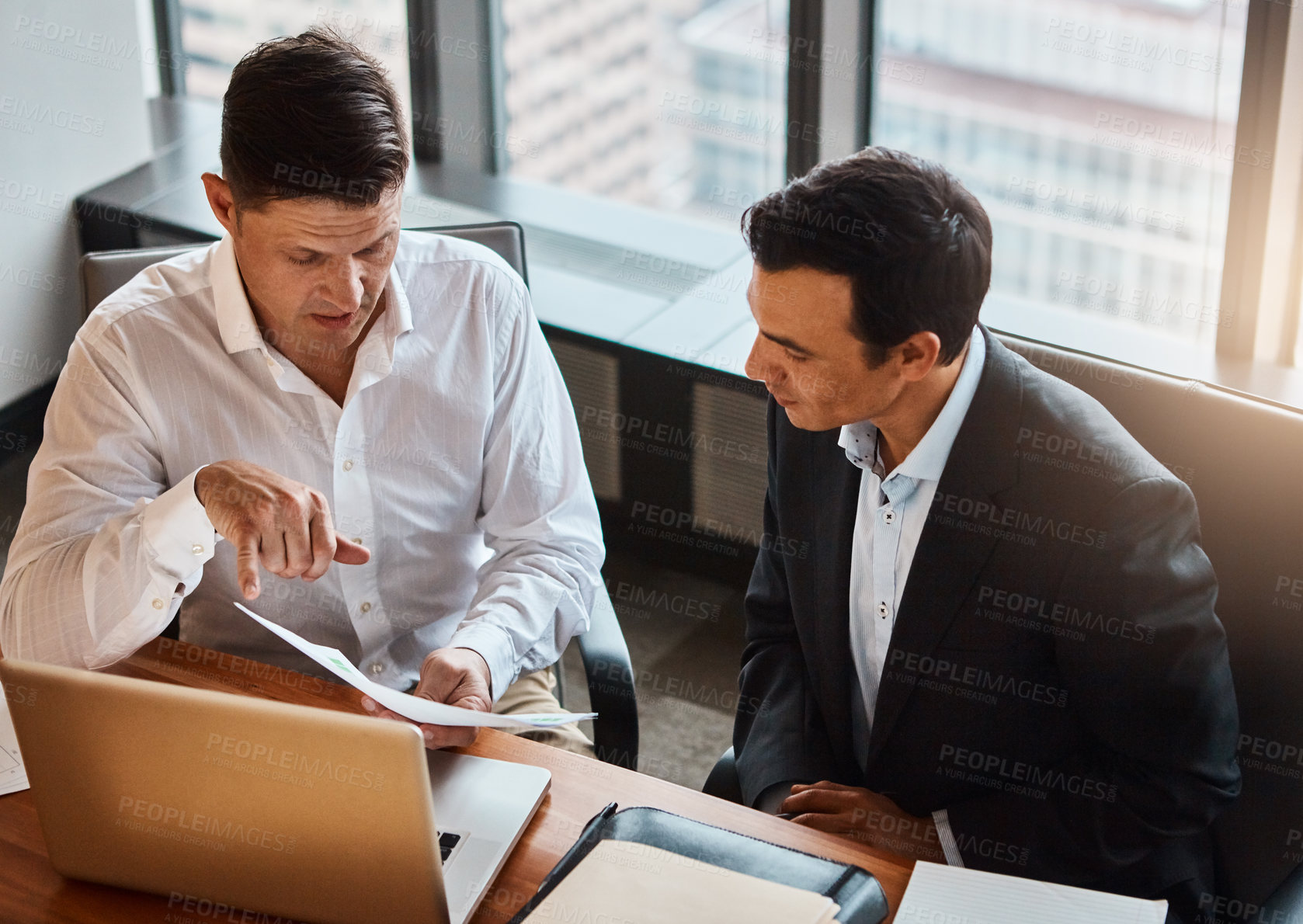 Buy stock photo Shot of two businessmen having a discussion while sitting by a laptop