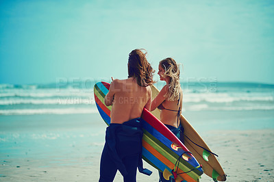 Buy stock photo Shot of a young couple walking on the beach with their surfboards