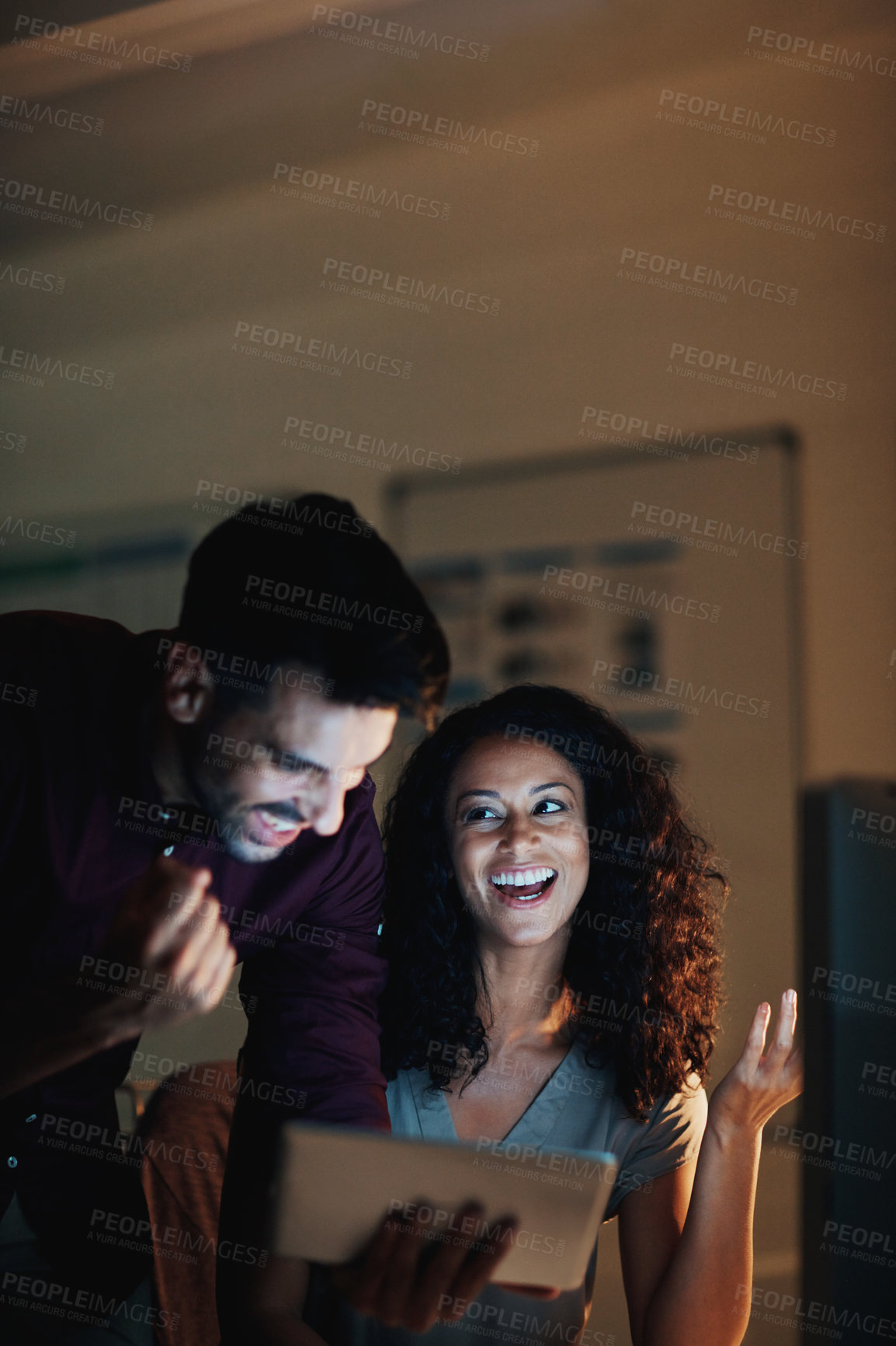 Buy stock photo Shot of two happy colleagues using a digital tablet together during a late night at work