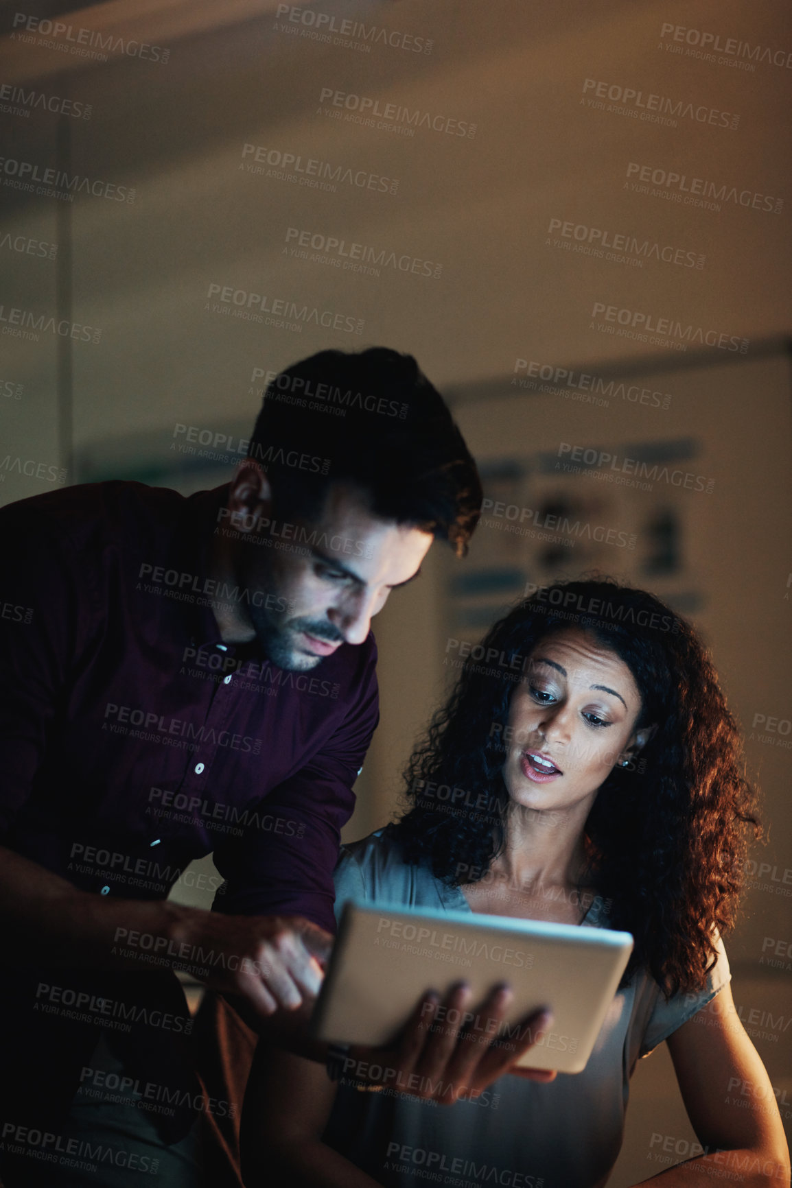 Buy stock photo Shot of two colleagues using a digital tablet together during a late night at work