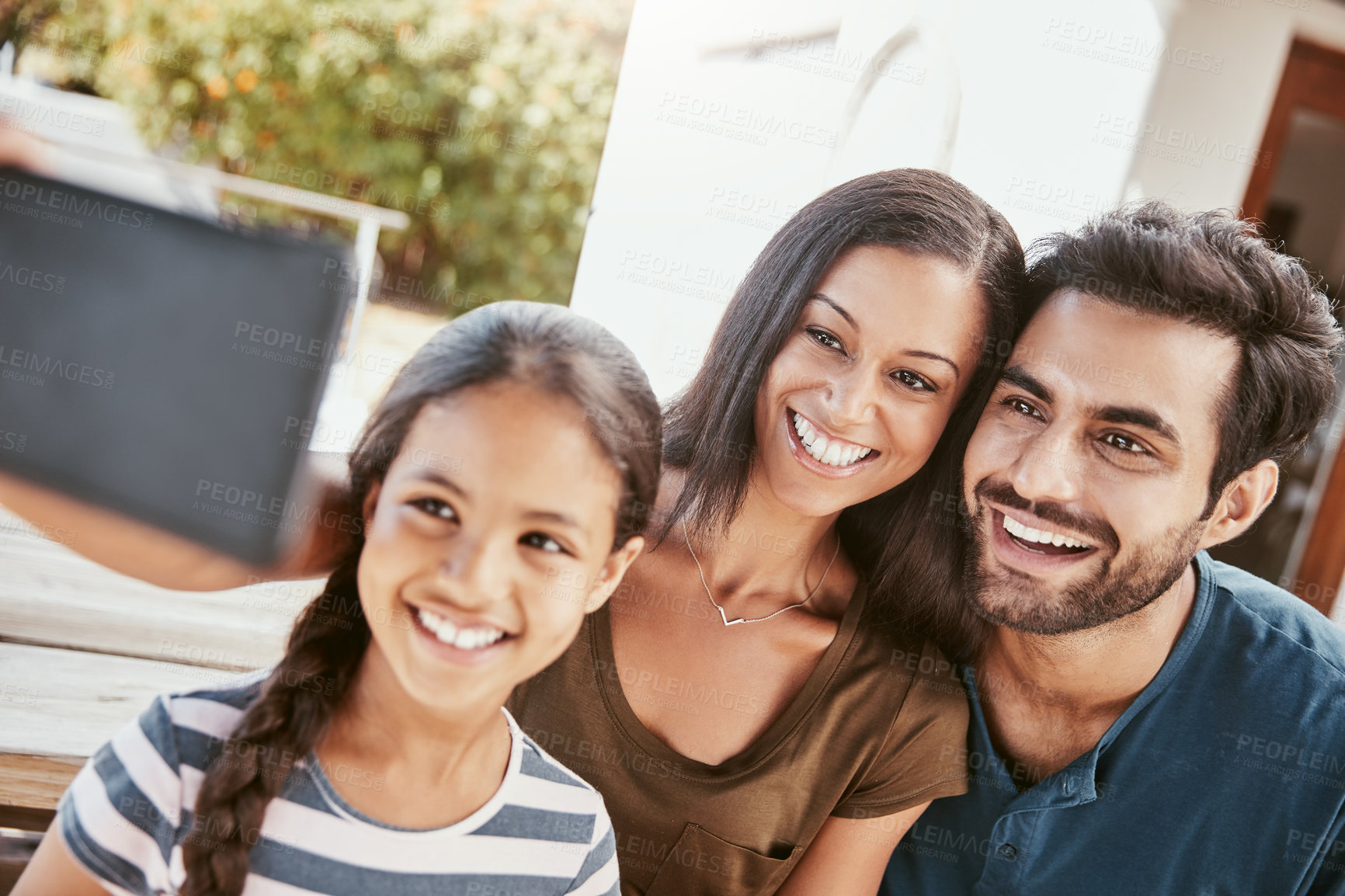 Buy stock photo Shot of a happy young family taking selfies together on a mobile phone