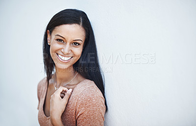 Buy stock photo Shot of a happy and attractive young woman leaning against a wall outside