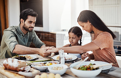 Buy stock photo Shot of a young family holding hands in prayer before having a meal together outdoors