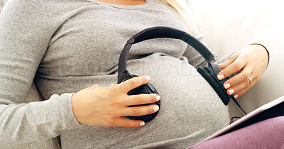 Buy stock photo Shot of a pregnant woman with headphones over her stomach at home