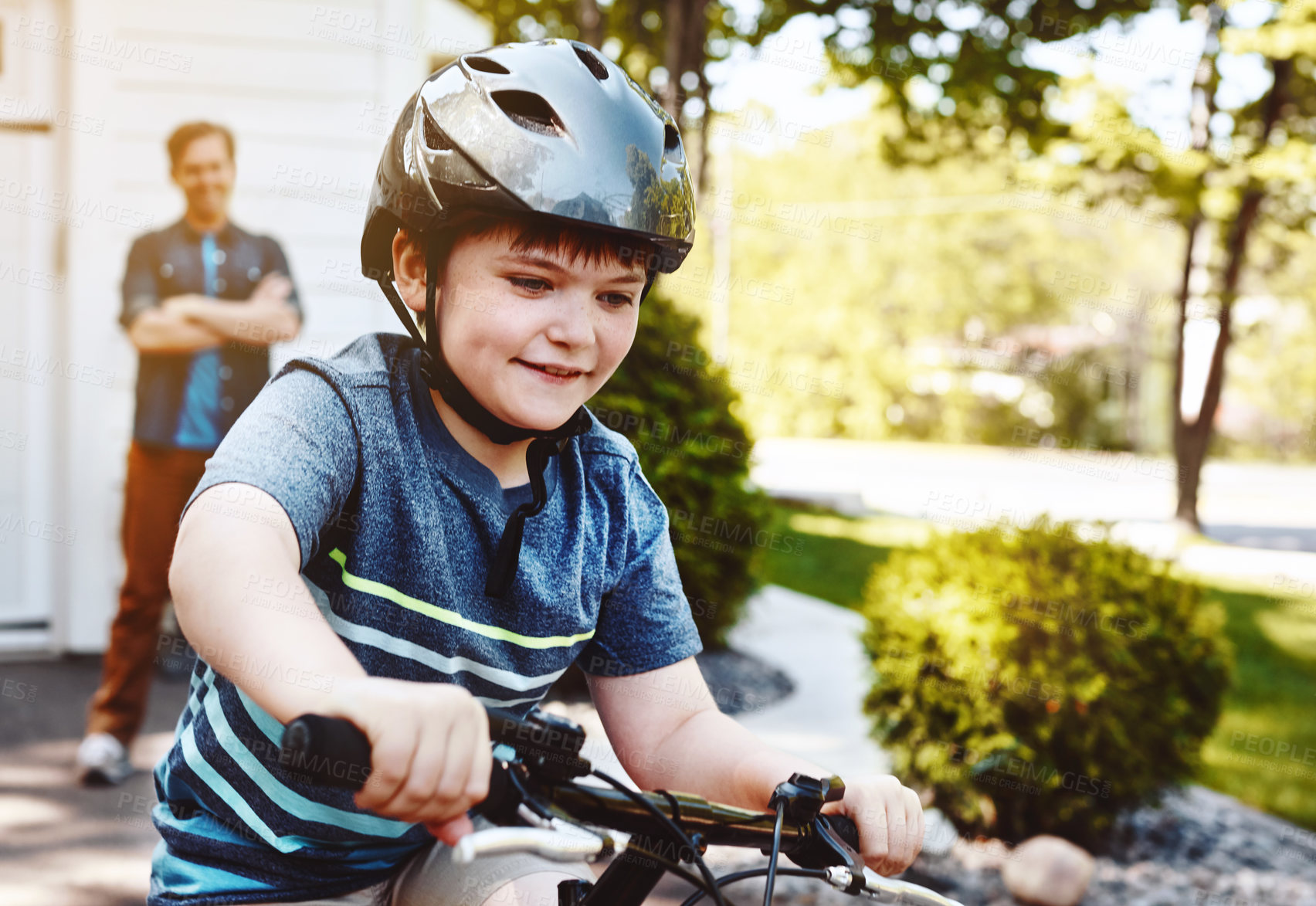 Buy stock photo Shot of a young boy riding a bicycle with his father in the background