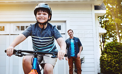 Buy stock photo Shot of a young boy riding a bicycle with his father in the background