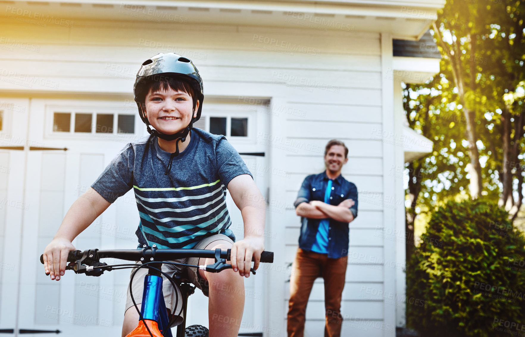 Buy stock photo Shot of a young boy riding a bicycle with his father in the background