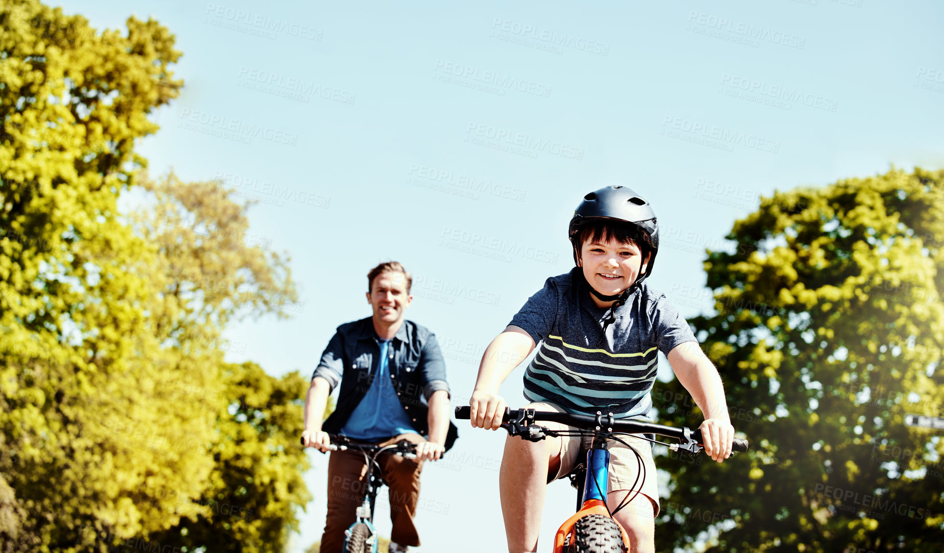 Buy stock photo Shot of a young boy and his father riding together on their bicycles