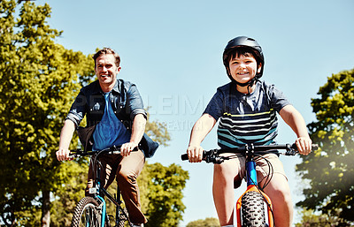Buy stock photo Shot of a young boy and his father riding together on their bicycles
