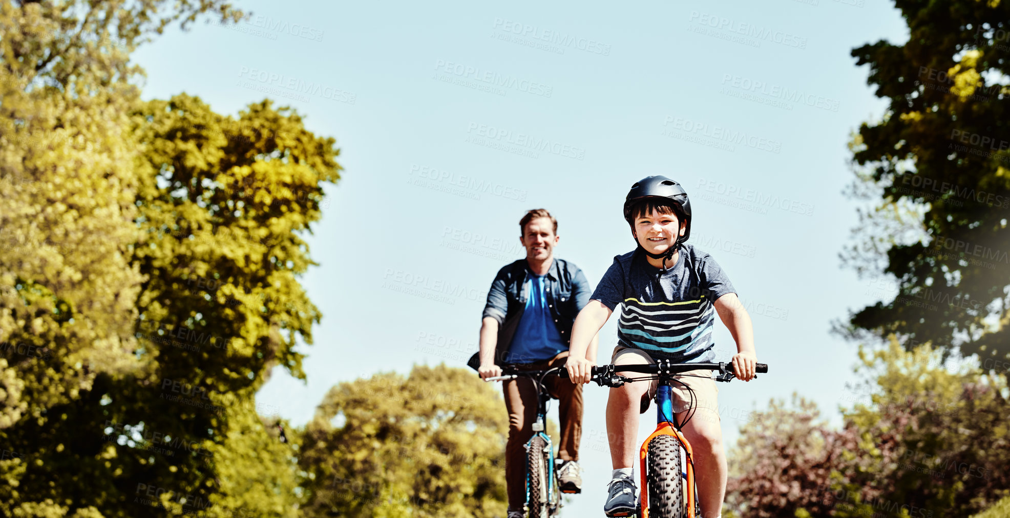 Buy stock photo Shot of a young boy and his father riding together on their bicycles