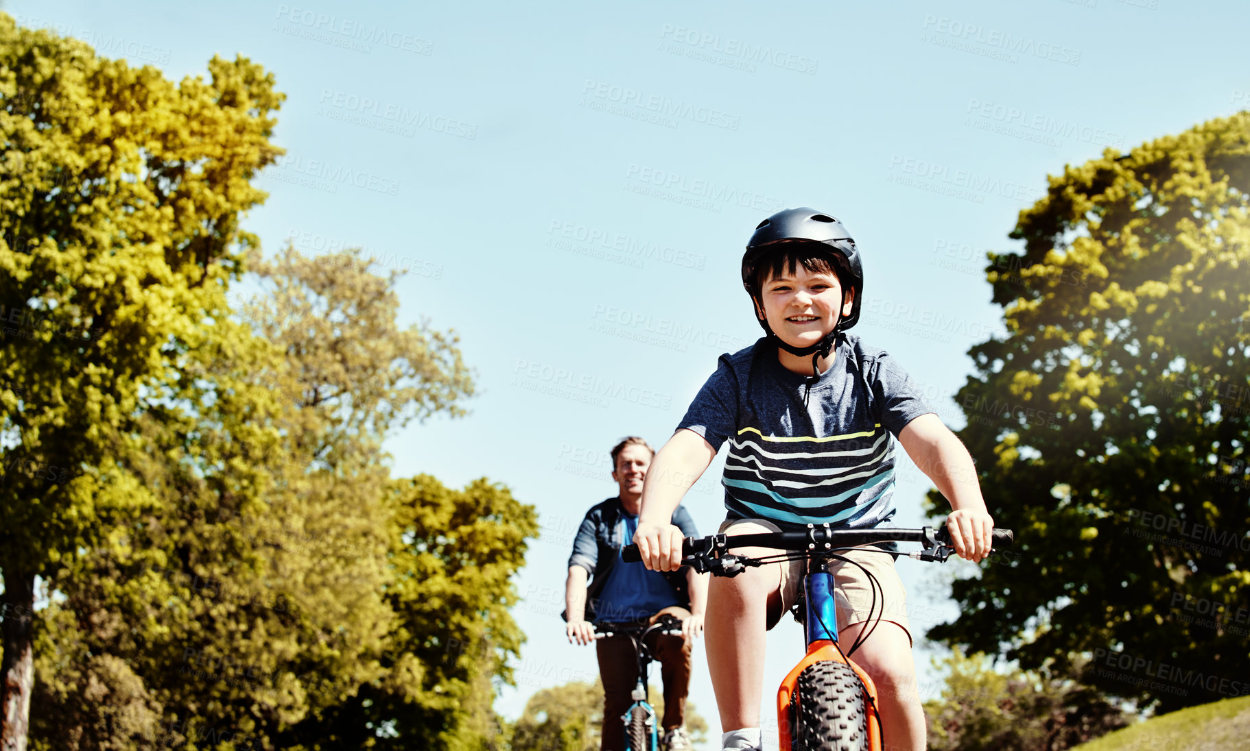 Buy stock photo Shot of a young boy and his father riding together on their bicycles