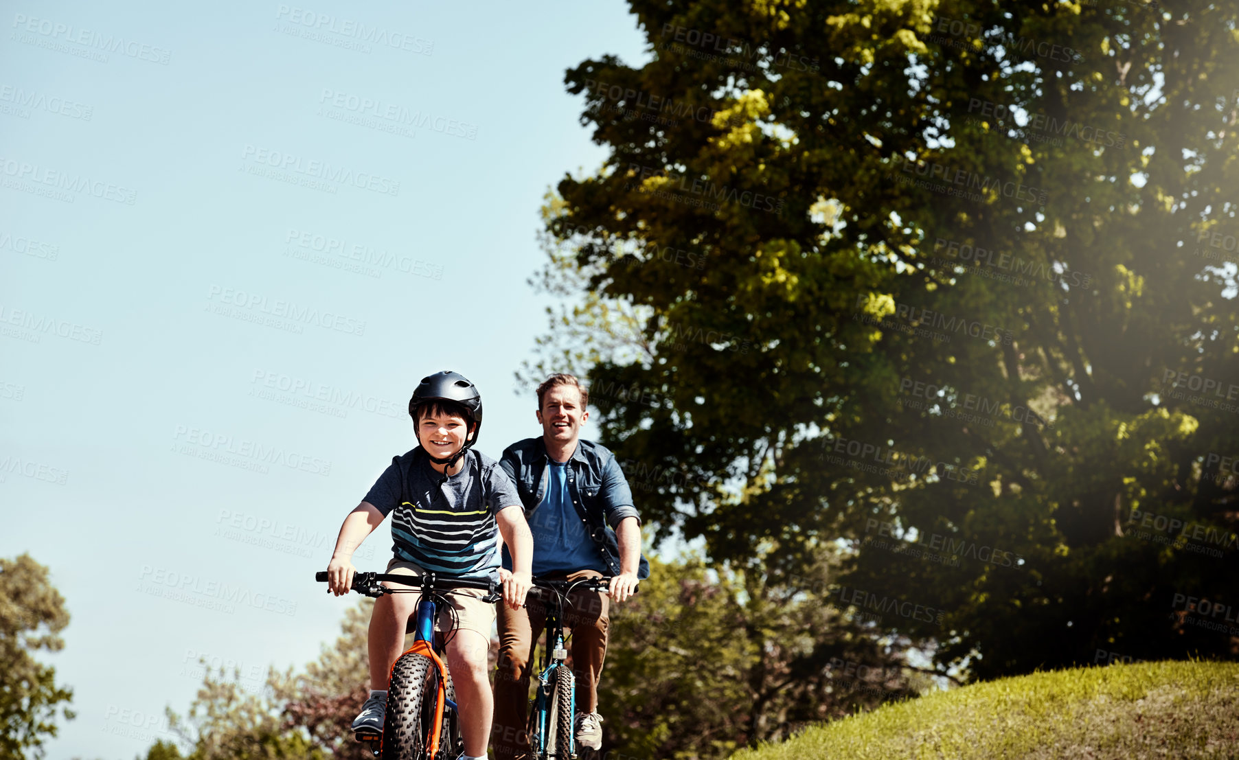 Buy stock photo Shot of a young boy and his father riding together on their bicycles