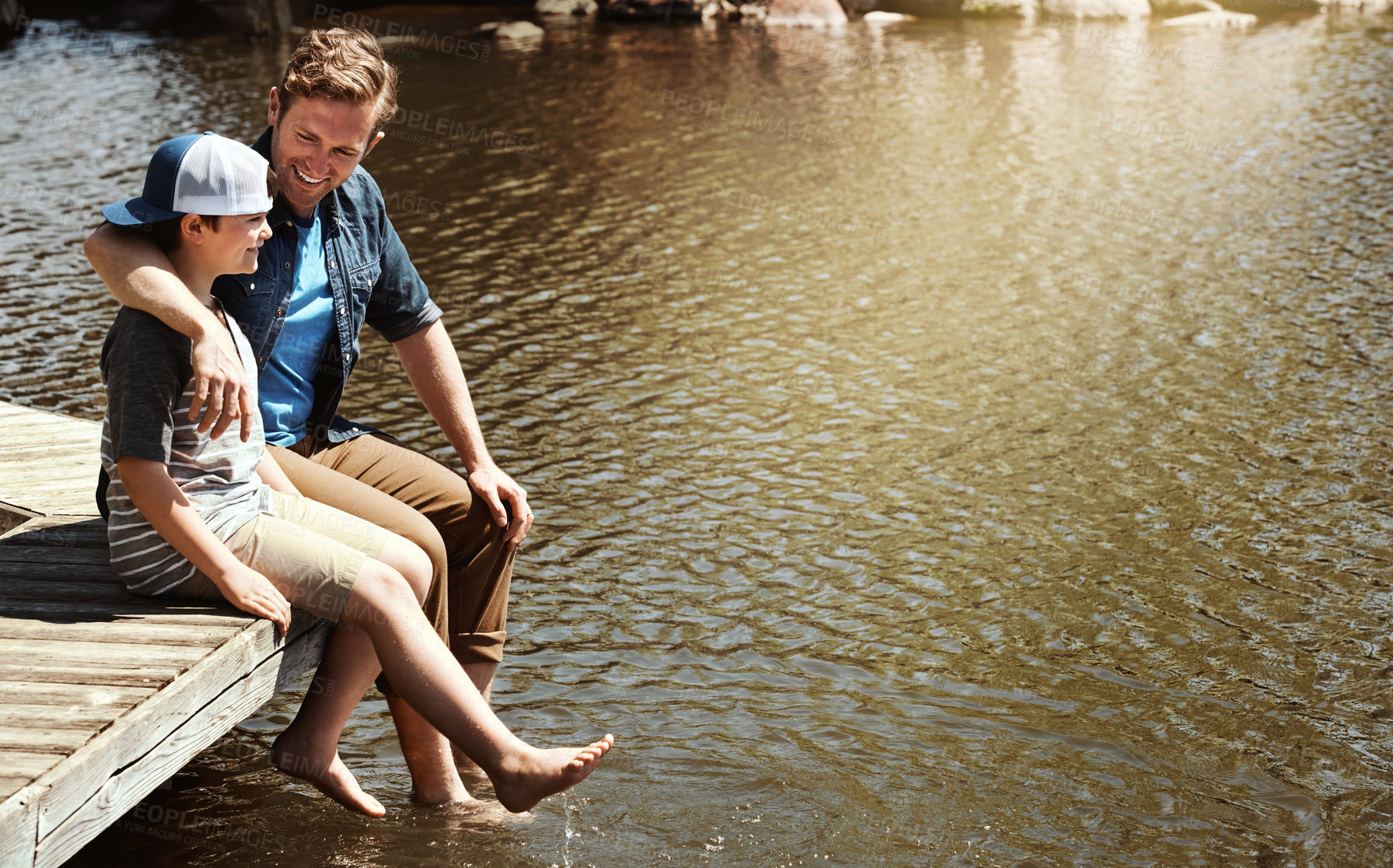 Buy stock photo Shot of a father and his little son sitting on a pier at a lake