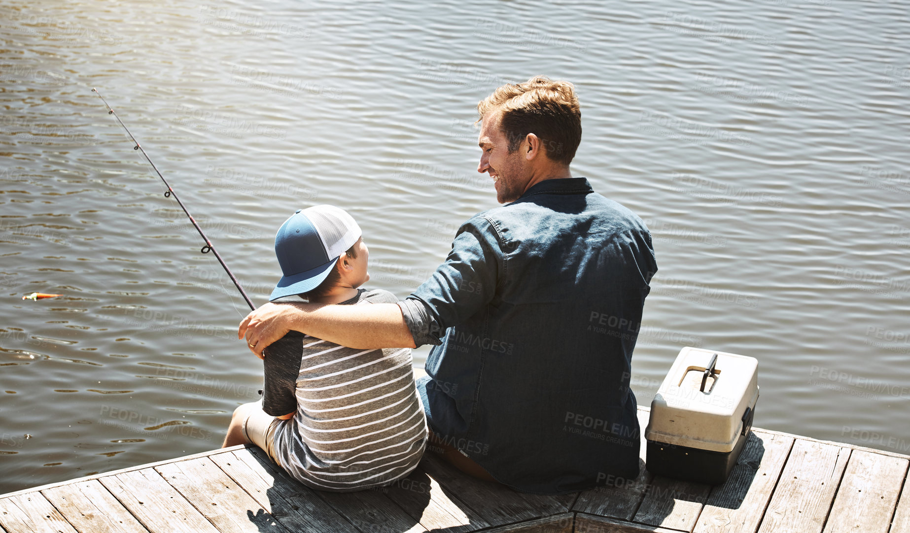 Buy stock photo Happy father, back view and fishing with son or rod by beach, lake or ocean in nature. Dad with child, kid or little boy enjoying bonding, lesson or tips to catch sea creatures with hug by water