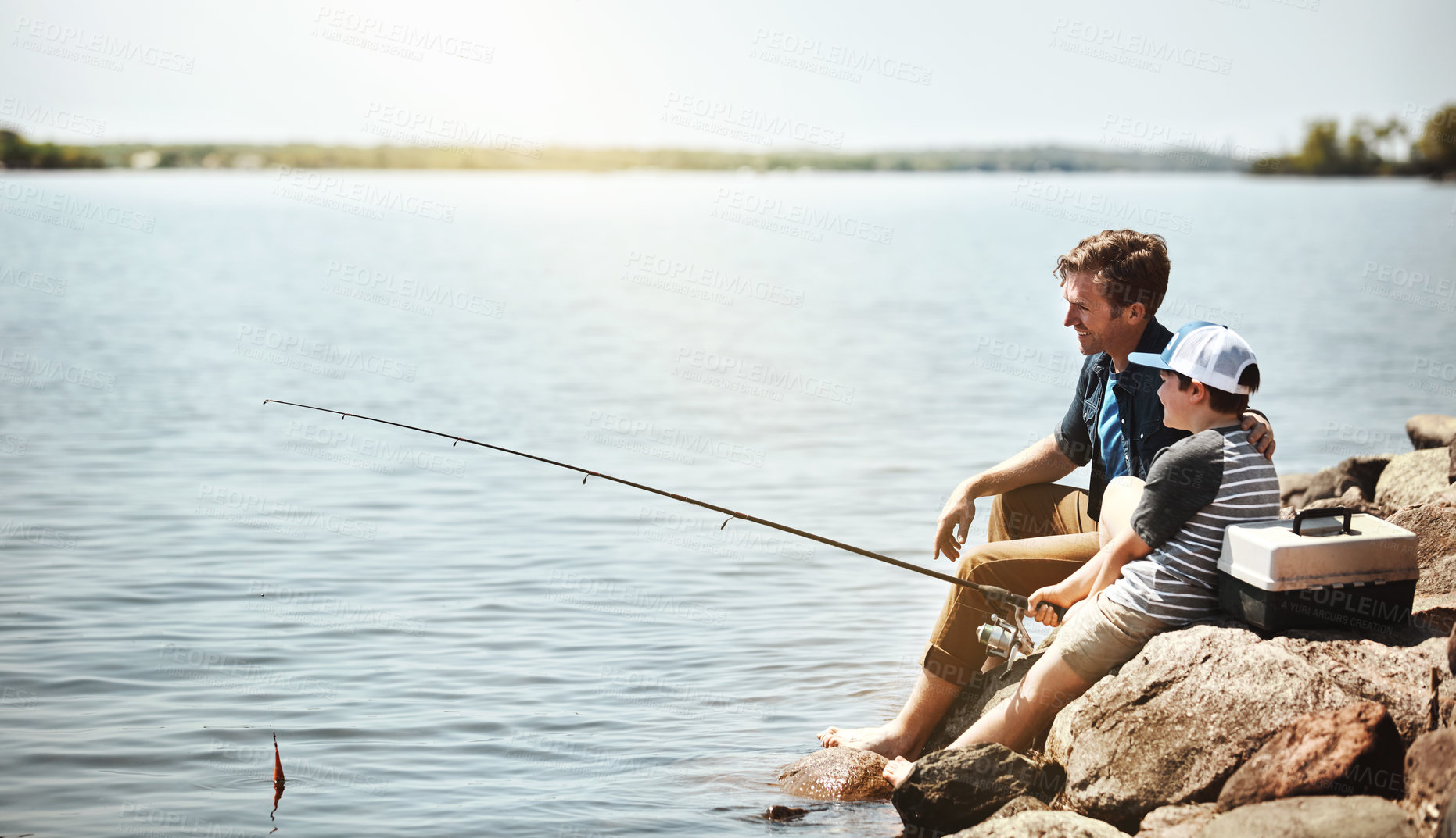 Buy stock photo Happy father, kid and fishing on rock with rod by lake, ocean or beach together in nature. Dad with son, young child or little boy with smile for bonding, lesson or teaching tip to catch by sea water