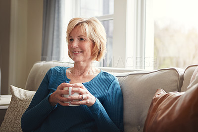 Buy stock photo Shot of a happy mature woman relaxing on the sofa with a warm beverage at home