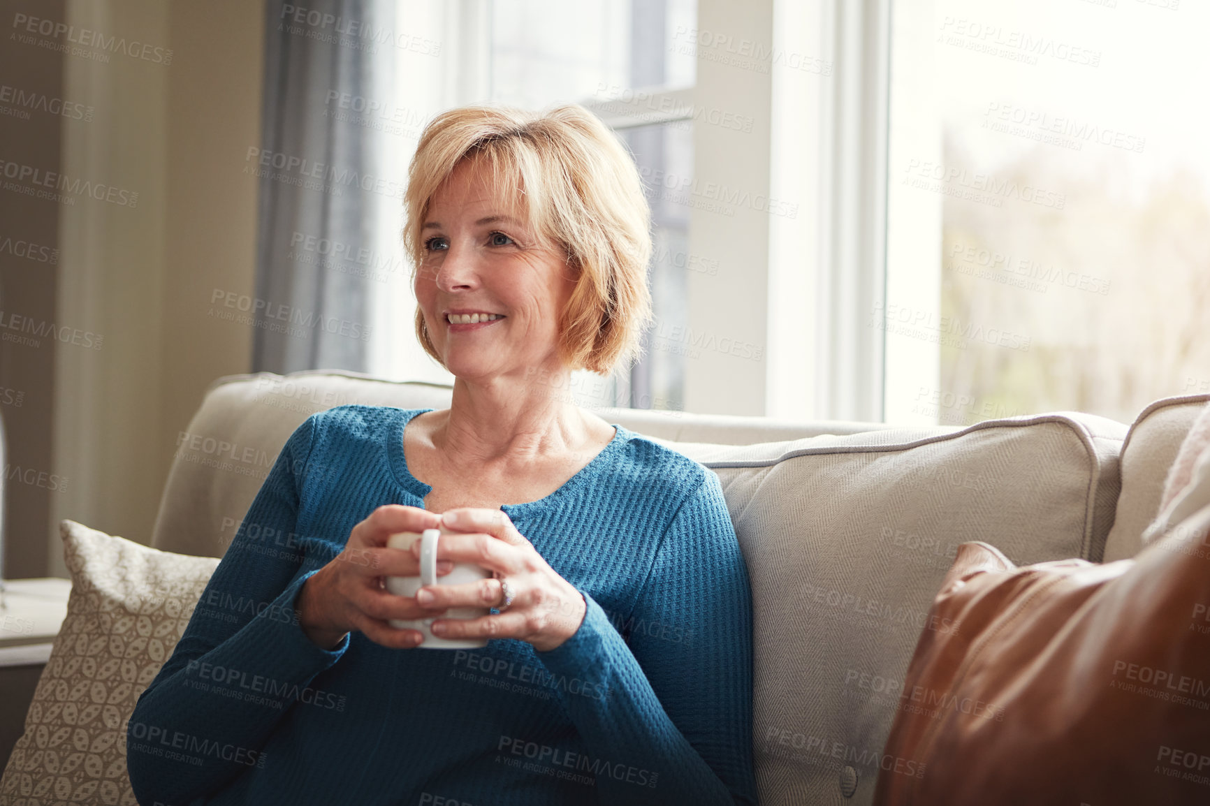 Buy stock photo Shot of a happy mature woman relaxing on the sofa with a warm beverage at home