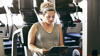 Buy stock photo Cropped shot of a sporty young woman looking at a digital tablet while sitting in the gym