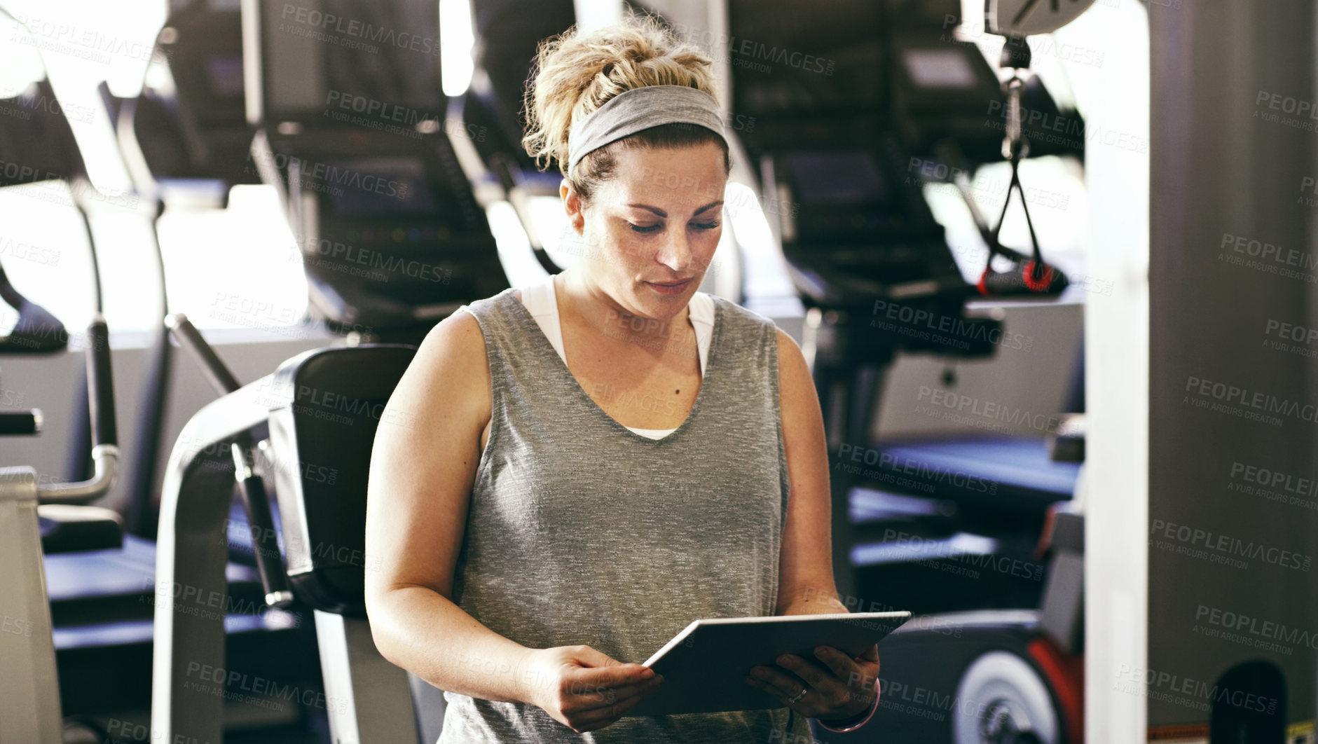 Buy stock photo Cropped shot of a sporty young woman looking at a digital tablet while sitting in the gym