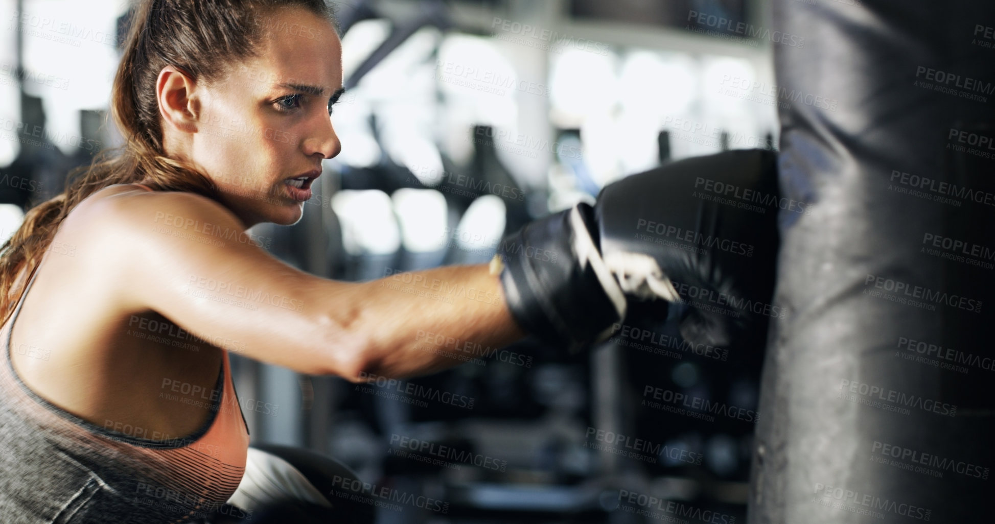 Buy stock photo Cropped shot of a young female boxer working out on a punching bag in the gym