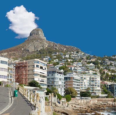 Buy stock photo Panorama of Lions Head seen from Sea Point, Cape Town, South Africa. A view of the peak of the lion's head surrounded by modern buildings and greenery with a blue sky. A pathway along the side. 
