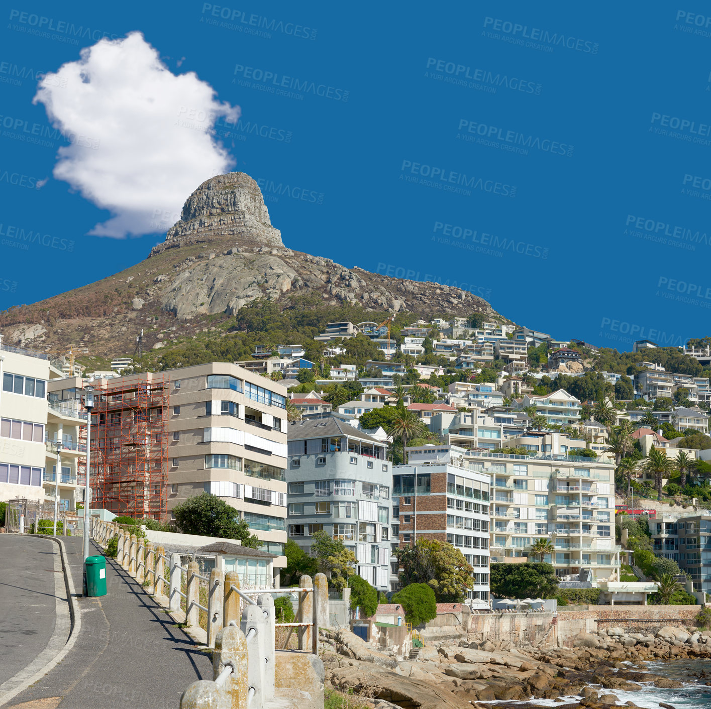 Buy stock photo Panorama of Lions Head seen from Sea Point, Cape Town, South Africa. A view of the peak of the lion's head surrounded by modern buildings and greenery with a blue sky. A pathway along the side. 