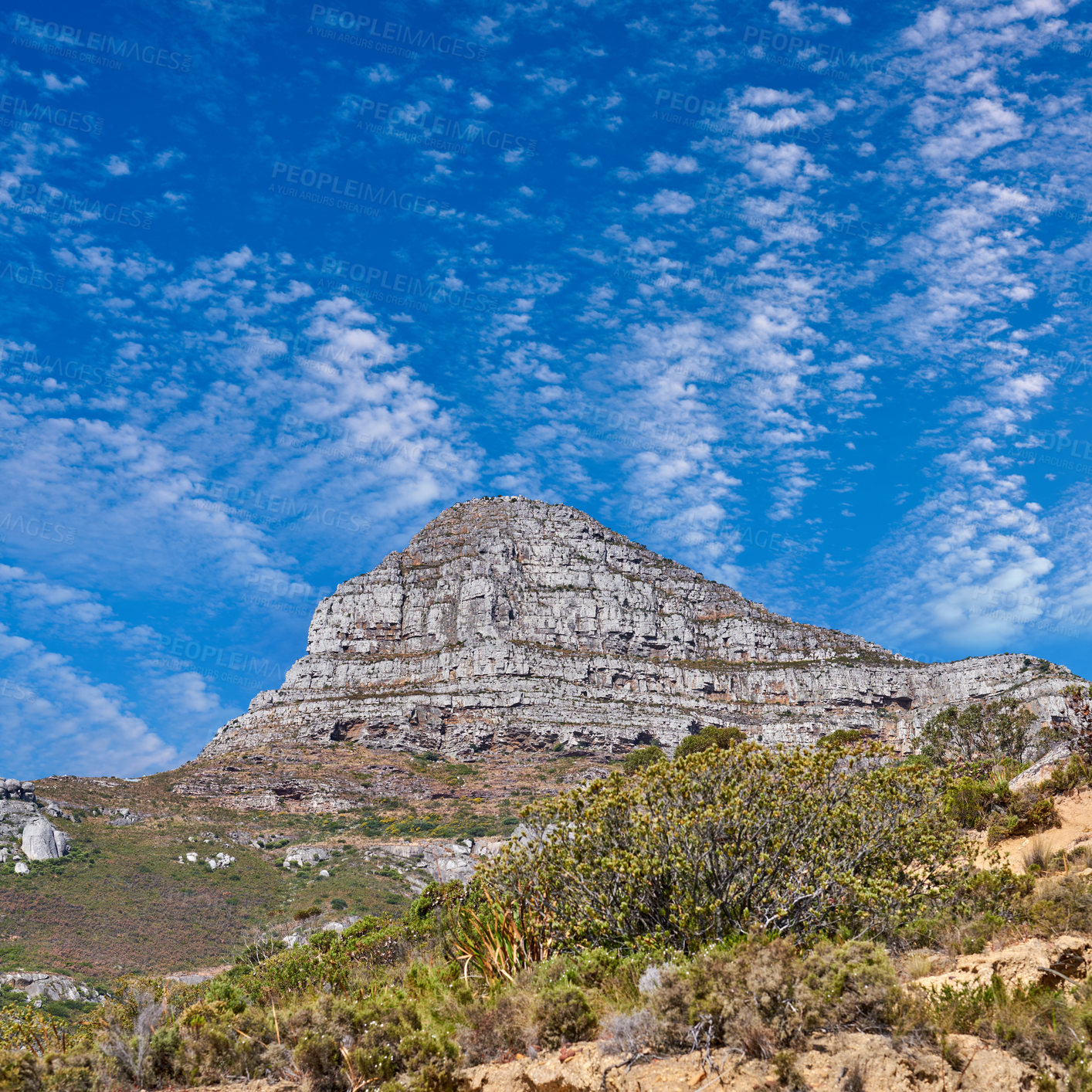 Buy stock photo Low angle landscape of Lions Head against a cloudy blue sky background. Rocky mountaintop with greenery in Cape Town, South Africa. Below view of popular tourist attraction and adventure hiking trail