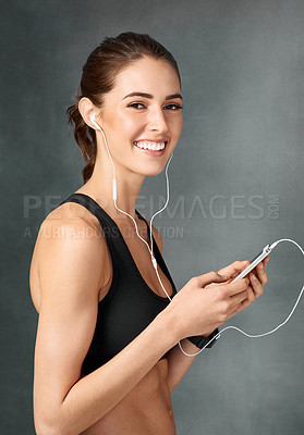 Buy stock photo Studio portrait of a sporty young woman listening to music against a grey background