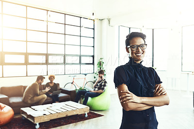 Buy stock photo Shot of a young designer standing in a office with her colleagues in the background