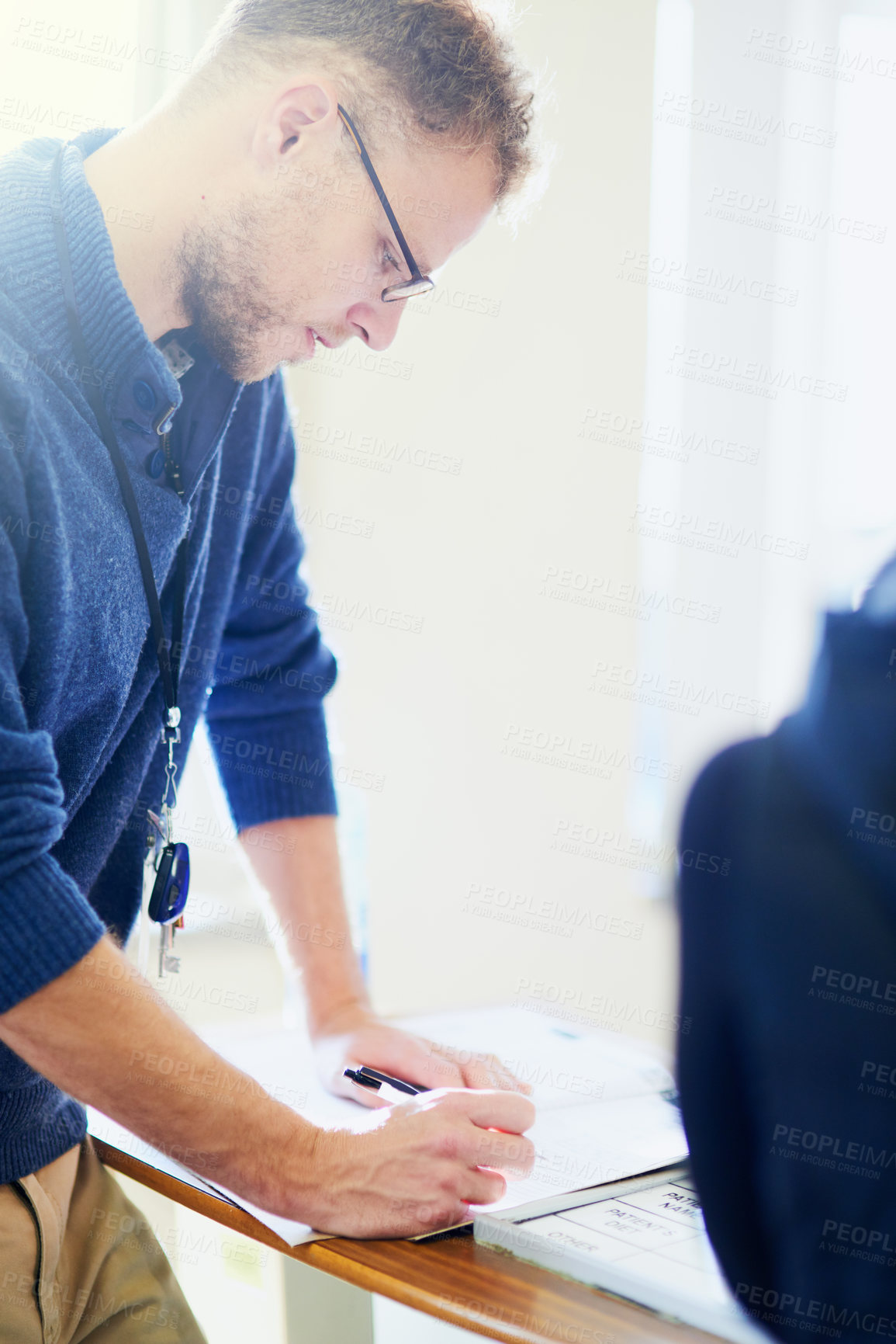 Buy stock photo Shot of a young doctor filling out paperwork in a hospital