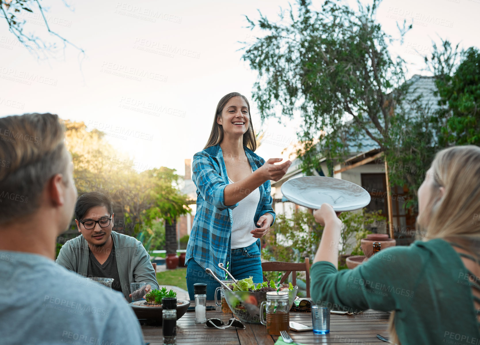 Buy stock photo Food, friends and dinner party on backyard patio with happy people and conversation at labor day lunch. Holiday, reunion and meal outside of home with salad, plates and care of host at social event