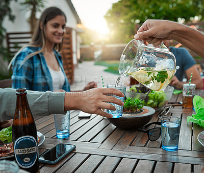 Buy stock photo Shot of two unrecognizable friends pouring water in a glass for each other outside around a table in a garden
