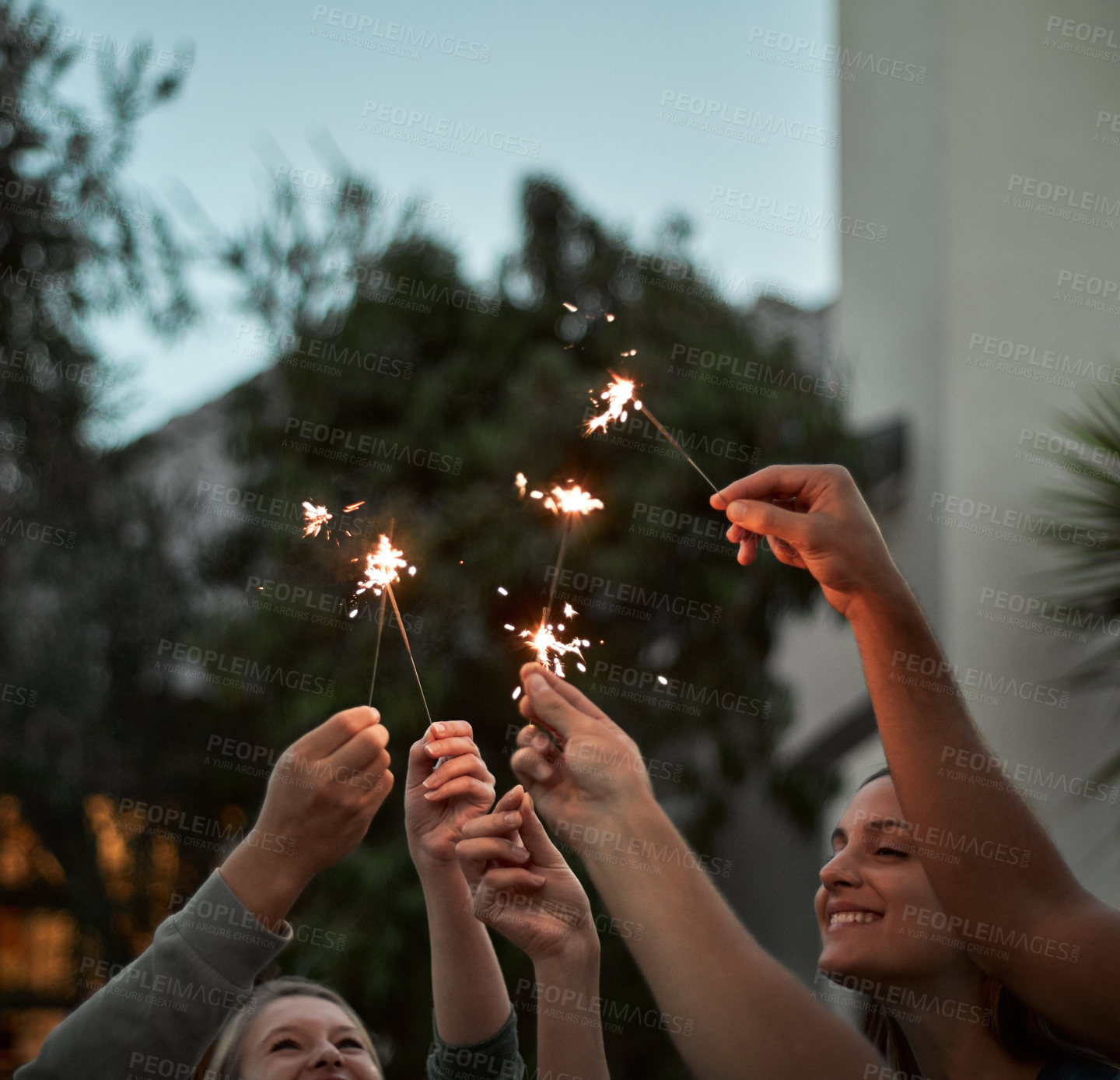 Buy stock photo Shot of a group of cheerful young friends each holding a sparkler in the air outside