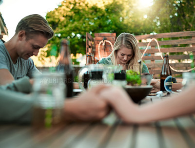 Buy stock photo Shot of a group of young friends holding hands together around a table outside in a garden