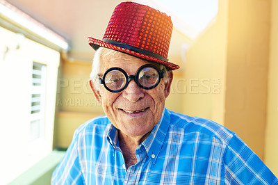 Buy stock photo Shot of a carefree elderly man wearing funky glasses and a hat while posing for the camera inside a building