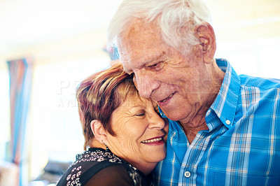 Buy stock photo Shot of a cheerful elderly couple holding each other and laughing while standing inside of a building