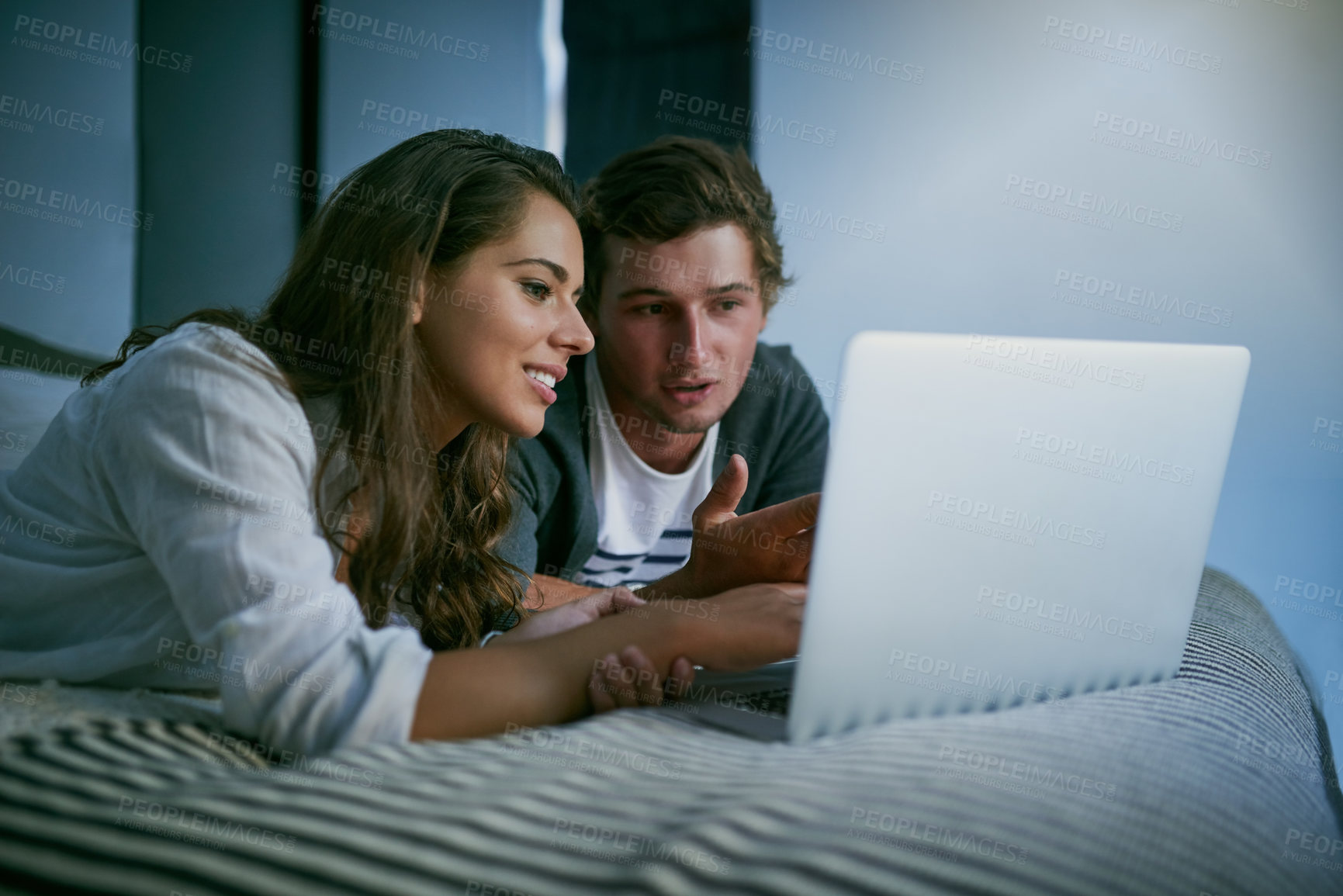 Buy stock photo Shot of a young couple using their laptop together while lying on bed