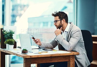 Buy stock photo Shot of a young businessman texting on his cellphone while working in an office