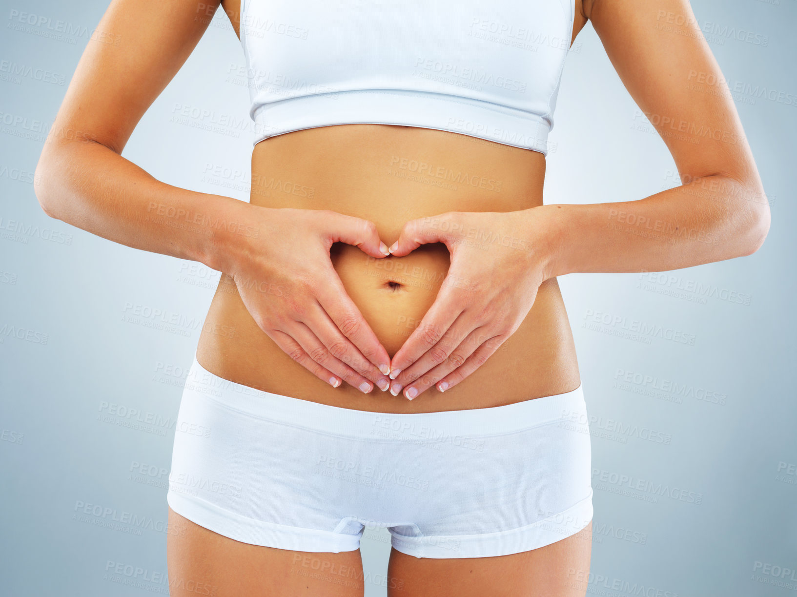 Buy stock photo Studio shot of an unrecognizable woman framing a heart on her stomach against a blue background