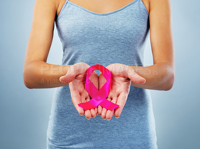 Buy stock photo Studio shot of an unrecognizable woman holding a breast cancer awareness ribbon against a blue background