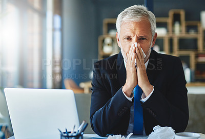 Buy stock photo Shot of a frustrated businessman using a tissue to sneeze in while being seated in the office