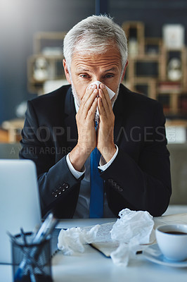 Buy stock photo Shot of a frustrated businessman using a tissue to sneeze in while being seated in the office