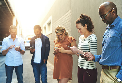 Buy stock photo Diverse group of adult people connecting and social networking outside. Businesspeople texting, browsing and sharing information on phones online while out of the office on a break from work.